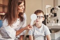 Now tell me what you see. Female doctor covers kid eye with medical tool for checking visual acuity