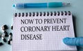 NOW TO PREVENT CORONARY HEART DISEASE - words on a white sheet on a light background with pen and tablets