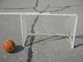 Noyabrsk, Russia - August 9, 2020: An orange-and-yellow basketball with a shadow next to a small soccer goal on the concrete floor