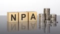npa - text on wooden cubes on a cold grey light background with stacks coins