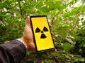 Nuclear atomic energy radiation warning sign on a smartphone screen in the green forest during summer.