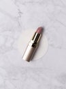 Nude pink lipstick in golden tube on creative marble background