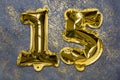 The number of the balloon made of golden foil, the number fifteen on a gray background with sequins.