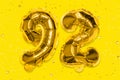 The number of the balloon made of golden foil, the number ninety-two on a yellow background with sequins. Royalty Free Stock Photo