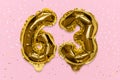 The number of the balloon made of golden foil, the number sixty-three on a pink background with sequins.