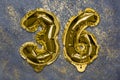 The number of the balloon made of golden foil, the number thirty-six on a gray background with sequins.