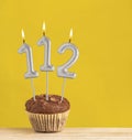 Number 112 birthday candle - Chocolate cupcake on a yellow background Royalty Free Stock Photo