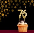 Number 76 birthday candle - Cupcake on black background with out of focus lights