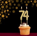 Number 74 birthday candle - Cupcake on black background with out of focus lights