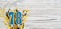 Number 78 blue celebration candle on white wooden background with golden foil. Copy space.