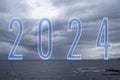 Number 2024 in blue tones on the horizon of the sea with cloudy sky, with reflection on the water. Royalty Free Stock Photo