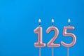 Number 125 - Burning anniversary candle on blue foamy background