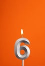 Number 6 - Burning anniversary candle on orange foamy background