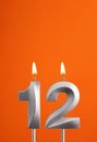 Number 12 - Burning anniversary candle on orange foamy background