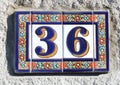 number 36 ceramic sign made of enamel or clay on a stone wall, blue-yellow thirty six with flowers