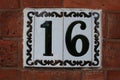 Number 16 door number Ceramic plate with black decorative boarder attached to a brick wall Royalty Free Stock Photo