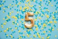 Number 5 five golden celebration birthday candle on yellow and blue confetti Background.