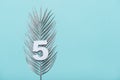 Number five shape with silver palm leaves on blue background. Summer concept. Flat lay. Top view