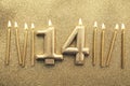 Number 14 gold celebration candle on a glitter background Royalty Free Stock Photo