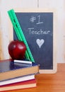 Number one teacher is written on a messy black chalkboard with old books in front. Royalty Free Stock Photo