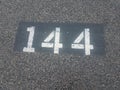 Number 144 painted on black asphalt or pavement