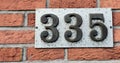 Number plate. Number 335 against a red brick wall background.