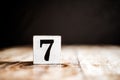 7 - Number 7 - Number Seven - White block with number on wooden table and dark background