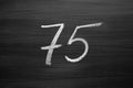 Number seventy five enumeration written with a chalk on the blackboard