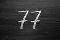 Number seventy seven enumeration written with a chalk on the blackboard