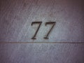 Number seventy seven or 77 made of metal. Sevens are unevenly distributed. On the wall