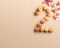 The number 2 shaped by apples and surrounded by colorful autumn leaves on a peach background.