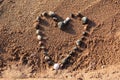 A heart made of snail seashells on the brown sand of the beach with shadows at sunset. Royalty Free Stock Photo