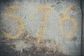 Numeral 576 yellow on a textured gray concrete wall with scratches and cracks. Royalty Free Stock Photo