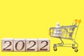 2022 numbers on wooden blocks next to a shopping cart carrying a wooden Christmas tree. The idea of Christmas shopping and Royalty Free Stock Photo