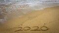 Numbers 2020 year on the sea shore, message handwritten in the golden sand on beautiful beach background Royalty Free Stock Photo