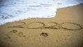 Numbers 2020 year on the sea shore, message handwritten in the golden sand on beautiful beach background Royalty Free Stock Photo