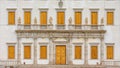 Numerous closed wooden windows, statues and a white door on the facade of an ancient historic building in Venetian style. Royalty Free Stock Photo