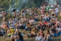 Numerous spectators sit on the slope of a picturesque hill and watch the performance of artists in the city park.