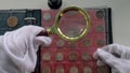 Numismatist examining old coin with magnifying glass closeup