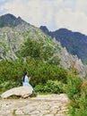 nun in blue clothes sits on a stone in the mountains. A religious person rests on a lonely hike along mountain trails