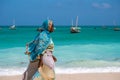 NUNGWI, ZANZIBAR - JAN 20, 2019: local woman in Bright Cloth walking by the Indian ocean Beach with a Bucket for Fish