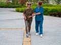 A nurse accompanies an elderly blind woman on a walk.