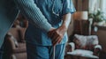 a nurse aids an elderly woman in standing up, their hands firmly gripping her walking stick, both dressed in a blue