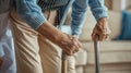 a nurse aids an elderly woman in standing up, their hands firmly gripping her walking stick, both dressed in a blue