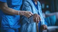 a nurse aids an elderly woman in standing up, their hands firmly gripping her walking stick, both dressed in a blue