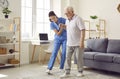 Nurse in assisted living facility holding elderly patient by hand and helping him walk