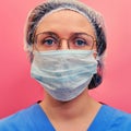 Nurse in a blue uniform and a protective mask on a red background. Portrait of a doctor woman in glasses and a medical hat, Royalty Free Stock Photo