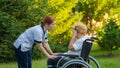 A nurse comforts a crying elderly caucasian woman in a wheelchair. Nurse walks with a patient in the park.