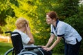 A nurse comforts a crying elderly caucasian woman in a wheelchair. Nurse walks with a patient in the park.