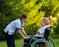 A nurse comforts a crying elderly caucasian woman in a wheelchair. Nurse walks with a patient in the park.